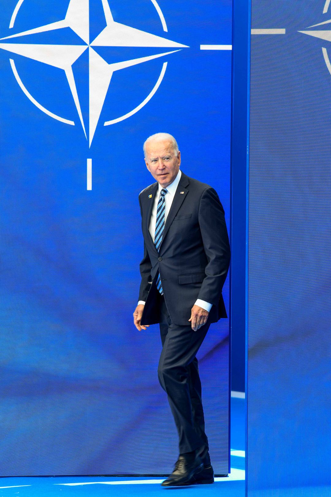 Biden kävelee estradille, taustalla Naton merkki.