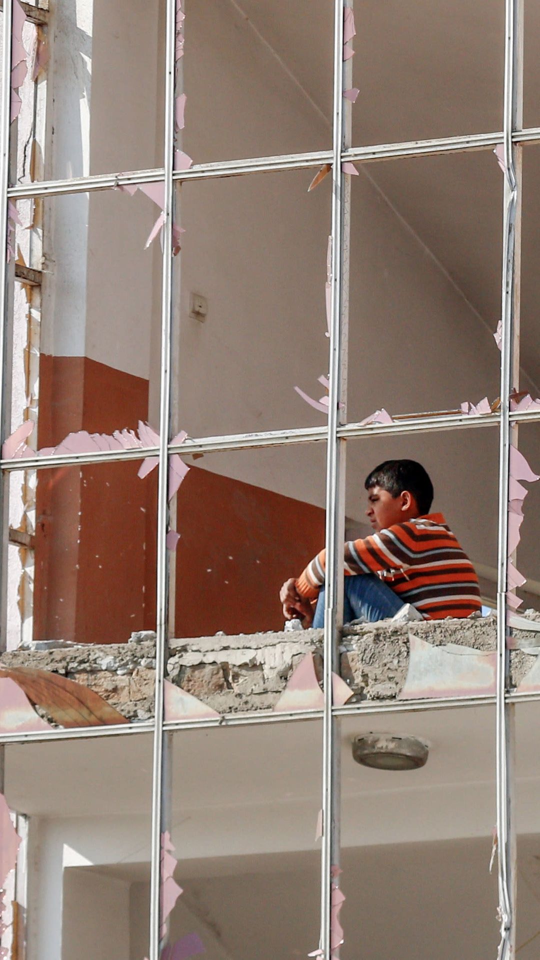 Nuori poika istuu raunioituneessa talossa, jonka ikkuna-lasit ovat säpäleinä. 