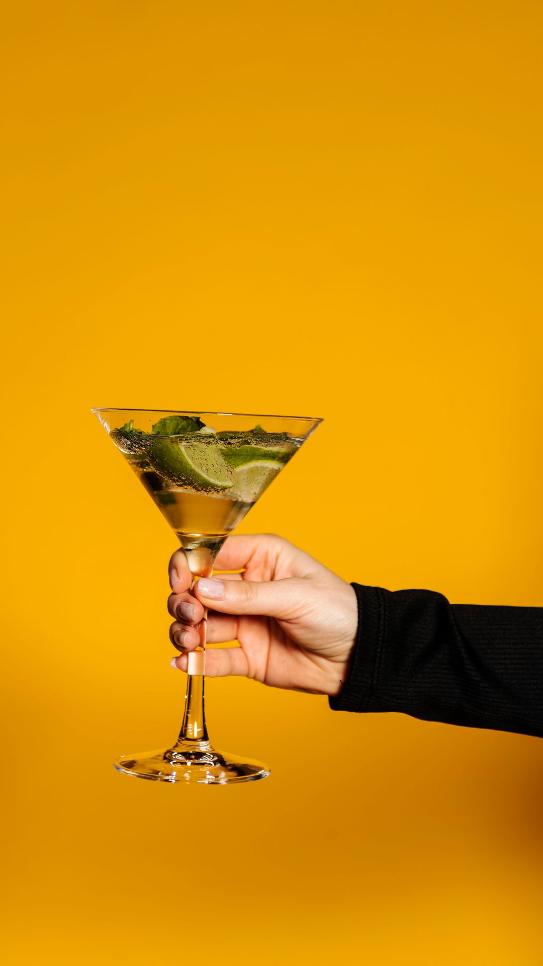 Wilma Tuominen pitelee kädessään drinkkilasia. Kuvassa drinkkilasi keltaisella taustalla.
