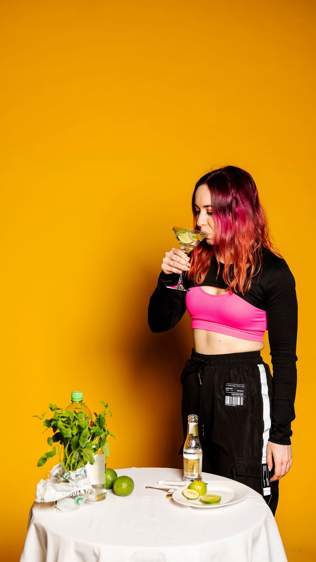 Wilma Tuominen juo drinkkilasista. Kuvassa on etualalla myös pöytä, jolla on minttua, limeä ja tonic-vettä.