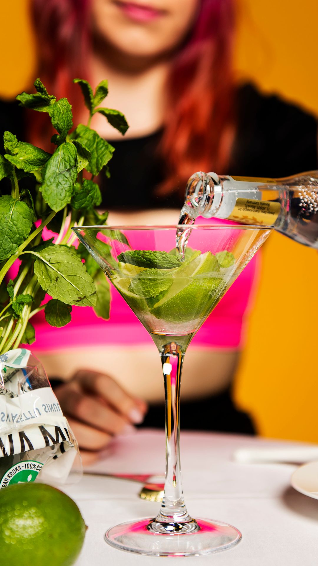 Wilma Tuominen kaataa drinkkilasiin tonic-vettä. Pöydällä on myös mintun lehtiä.