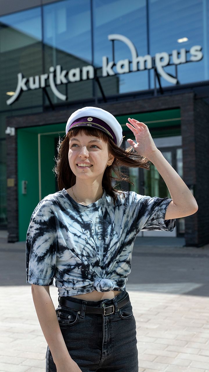 Minni Pitkämö ylioppilaslakki päässä kampuksen edessä