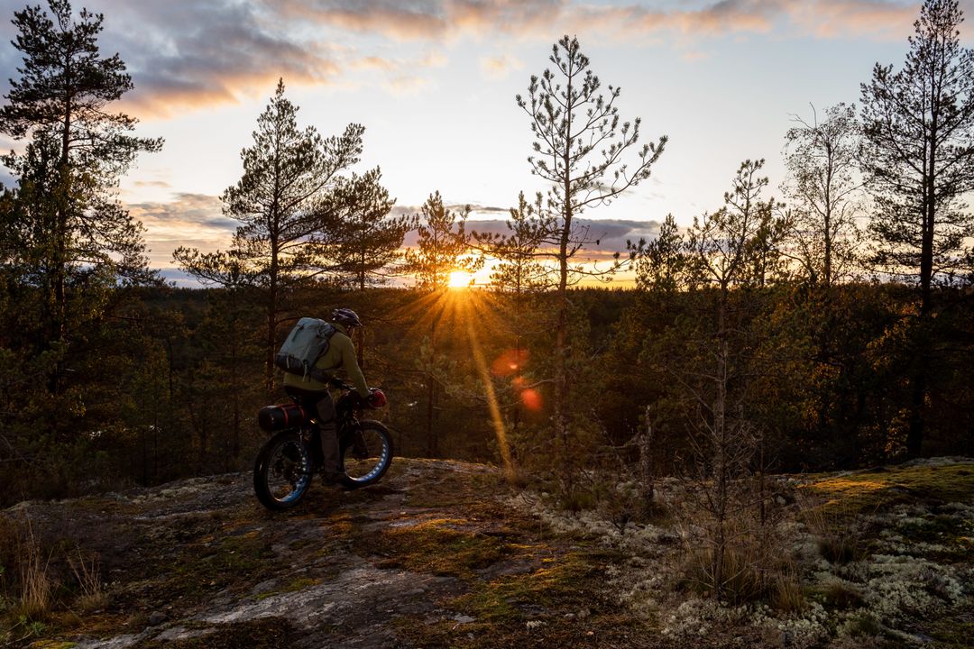 Polkupyöräilijä auringonlaskiessa kallion päällä metsässä.